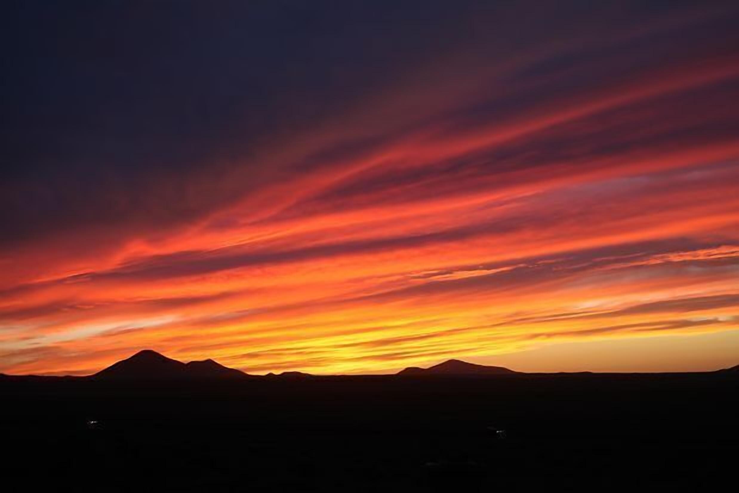 Silueta de una cordillera contra un cielo de atardecer con tonos rojos y naranjas vibrantes.