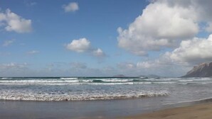 Une plage avec des vagues, un ciel dégagé et des montagnes à l’horizon.