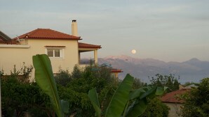 A house with a red-tiled roof, a chimney, and a balcony. In the background, there are mountains and a full moon. - Fantastic villa with a swimming pool ideal for a relaxing vacation and more... (Messini, Messinia)