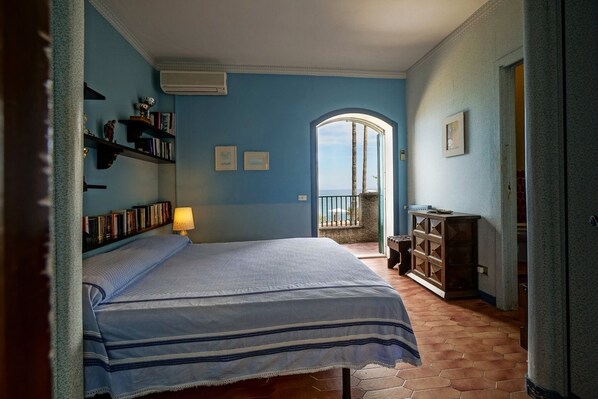 A bedroom with a bed, bookshelves, a lamp, a wooden cabinet, and a view through an arched doorway.