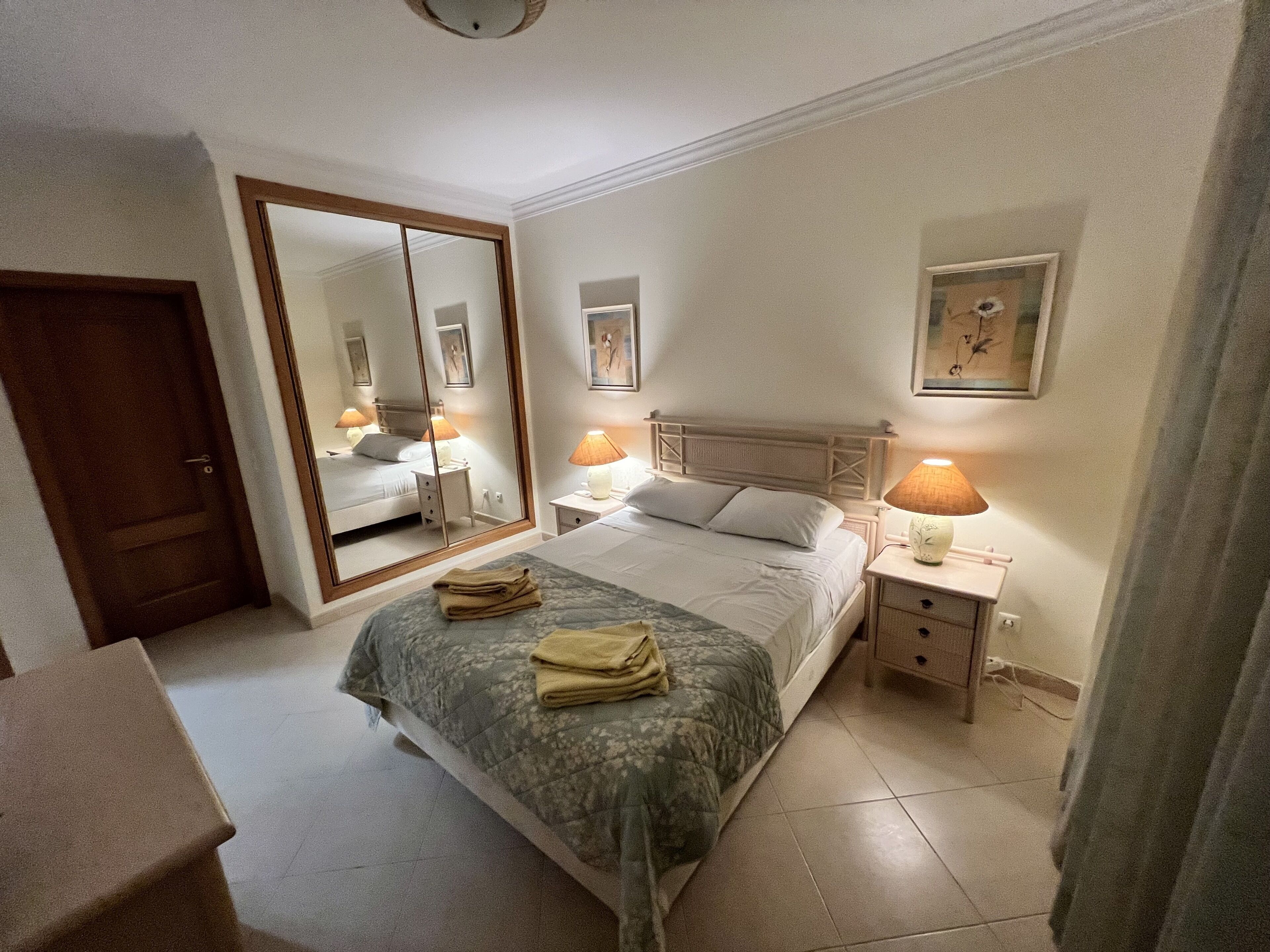 A hotel room with a large bed, bedside tables with lamps, a mirror, and a door.
