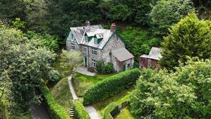A stone house with a green roof, surrounded by lush greenery and a winding path. - Large Period House set in Ancient Woodland in Exmoor National Park near Lynmouth (Lynton)