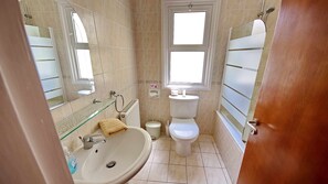 Bathroom features a sink, toilet, and glass shower enclosure, with a window above the toilet and a mirror above the sink.