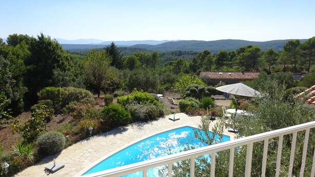 Una piscina con terraza de piedra, rodeada de exuberante vegetación y vistas a montañas distantes.