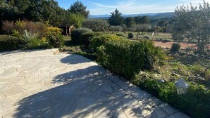 Un patio de piedra con vista a un jardín ajardinado y colinas al lejano.