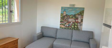 A room with a grey sofa, a wooden dresser, and a painting of a town on the wall.