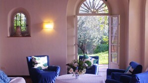 A room with two blue armchairs, a white table, and a view of a garden through an open door. - 'Stunning Views': beachfront villa with pool (Garda)