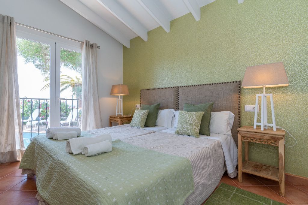 Ein Hotelzimmer mit einem großen Bett, zwei Nachttischlampen, Blick ins Freie und einem Balkon.