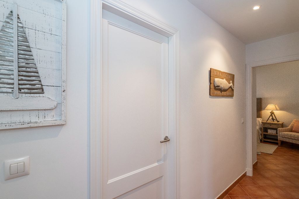 A hallway with a white door, a wall-mounted picture of a sailboat, and a welcome sign with a whale.