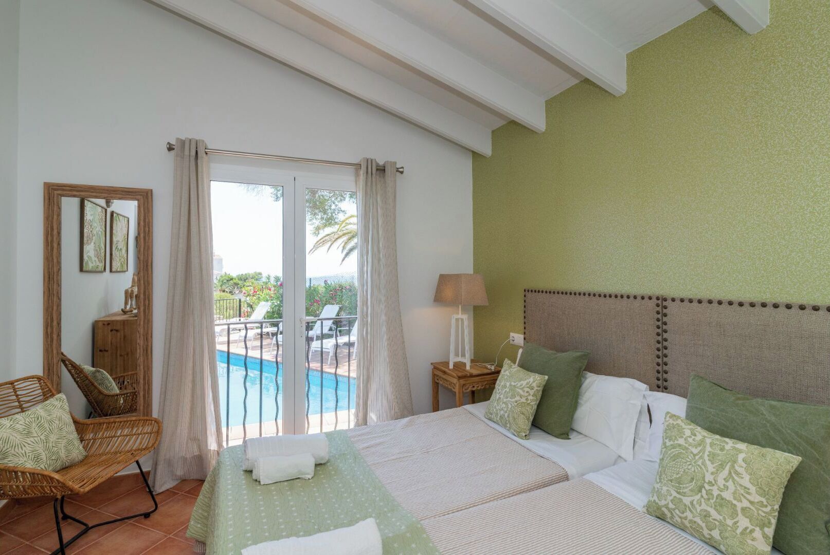 Ein Hotelzimmer mit Bett, Stuhl, Nachttisch, Lampe und Blick auf einen Swimmingpool.