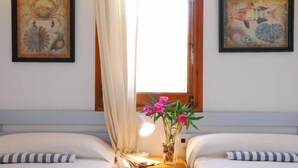 Une chambre d’hôtel avec deux lits, une fenêtre avec des rideaux et deux œuvres d’art encadrées accrochées aux murs.