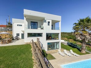 Une maison moderne à deux étages, dotée d’une piscine, d’un espace extérieur aménagé et offrant une vue sur le paysage environnant.