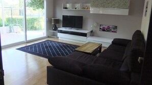 A modern living room with a dark sofa, a flat-screen TV, a coffee table, and a sliding glass door leading to a balcony. - Villa villa lLa Serreta (Alicante)