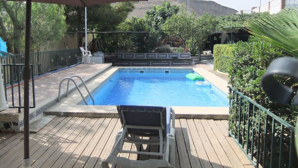 A swimming pool with a wooden deck, a lounge chair, and a large umbrella. - Villa villa lLa Serreta (Alicante)