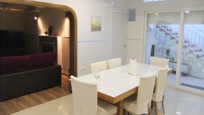 A modern dining area with a white table and chairs, a dark sofa, and a wooden accent wall. - Villa villa lLa Serreta (Alicante)