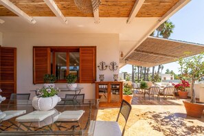 A covered outdoor patio with a table and chairs, potted plants, and a wooden ceiling.