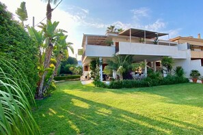 A modern two-story house with a flat roof, surrounded by lush greenery and a well-maintained lawn.