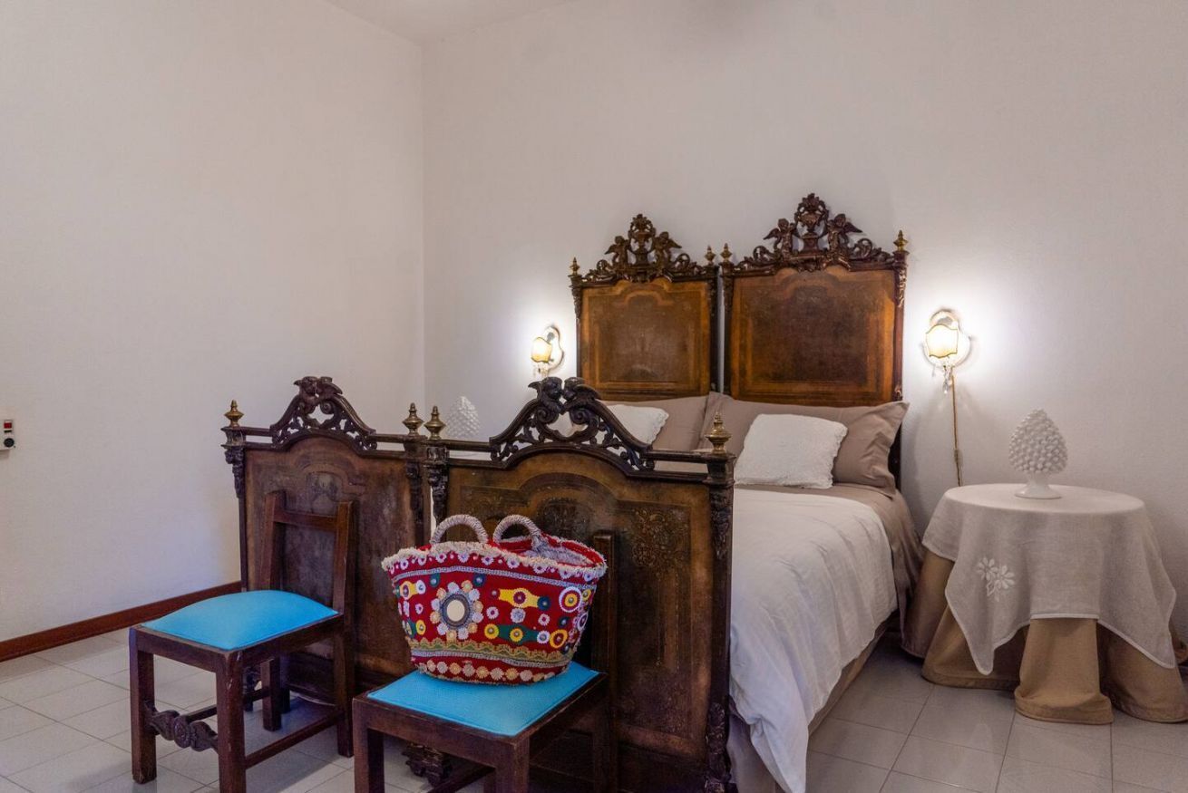 Une chambre à coucher avec une tête de lit en bois, un lit recouvert d’une literie blanche, une petite table recouverte d’une nappe blanche et un panier décoratif posé sur une chaise.