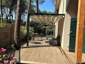 Une terrasse en bois avec des meubles d’extérieur, une pergola et une porte verte.