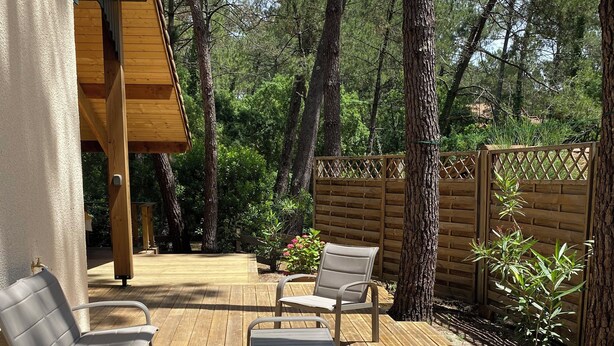 Une terrasse en bois, agrémentée de mobilier d’extérieur, entourée d’arbres et d’une clôture en bois.