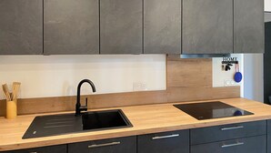Une cuisine moderne avec des meubles de couleur sombre, un évier noir et une plaque de cuisson à induction intégrée.