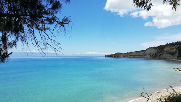 A coastal beach with clear turquoise water, a sandy shore, and a distant cliff. - Elia apartment Holiday paradise next to the beach (Agia Triada, Koroni, Messinia)