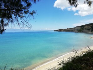 Una playa costera con agua turquesa cristalina, una orilla arenosa y un acantilado distante.