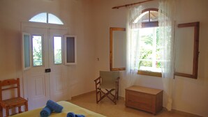 A bedroom with a bed, a chair, a wooden chest, and a window with curtains. - Elia apartment Holiday paradise next to the beach (Agia Triada, Koroni, Messinia)