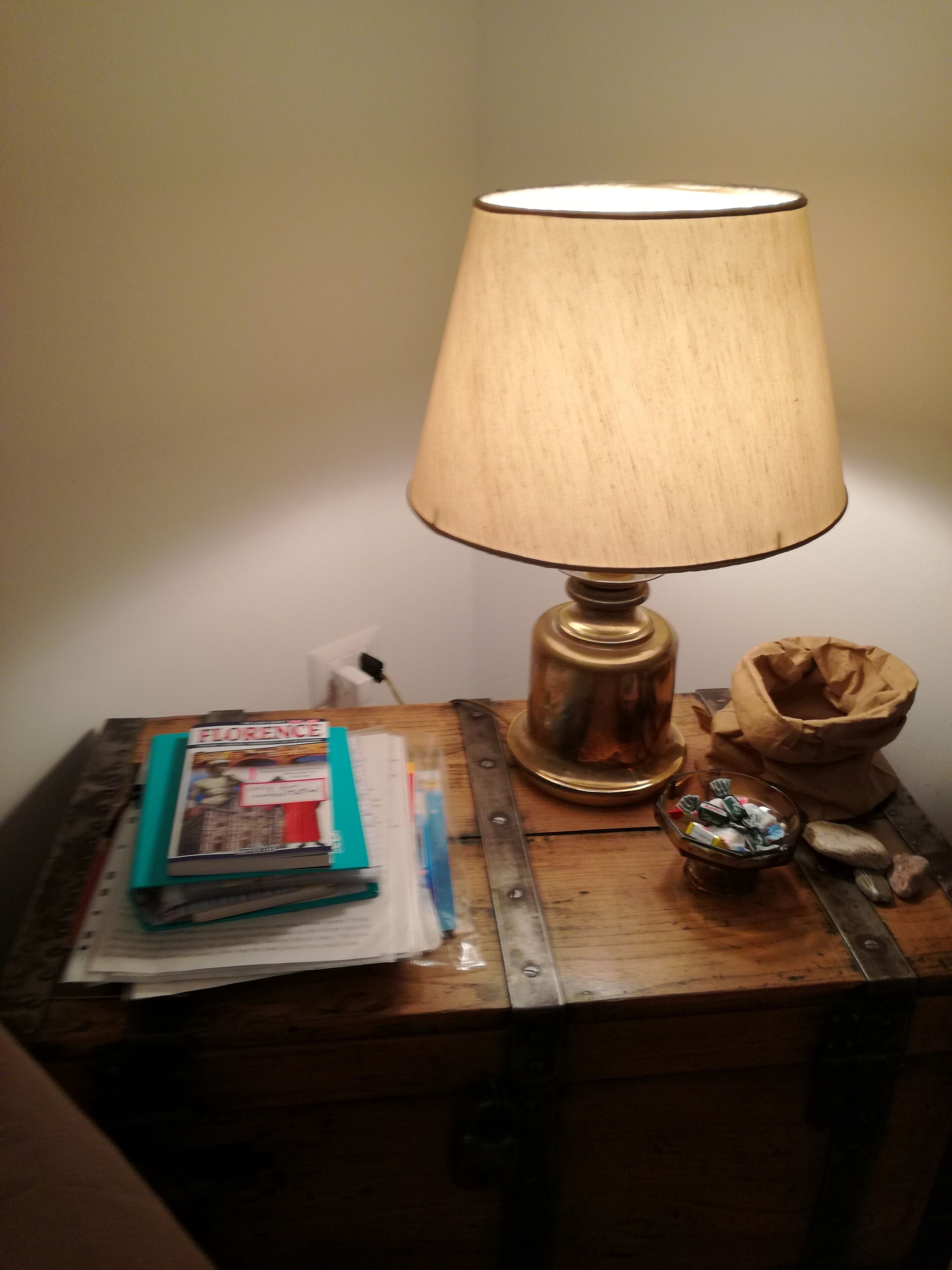 A wooden nightstand with a lamp, a book, a glass jar, and a small bowl.