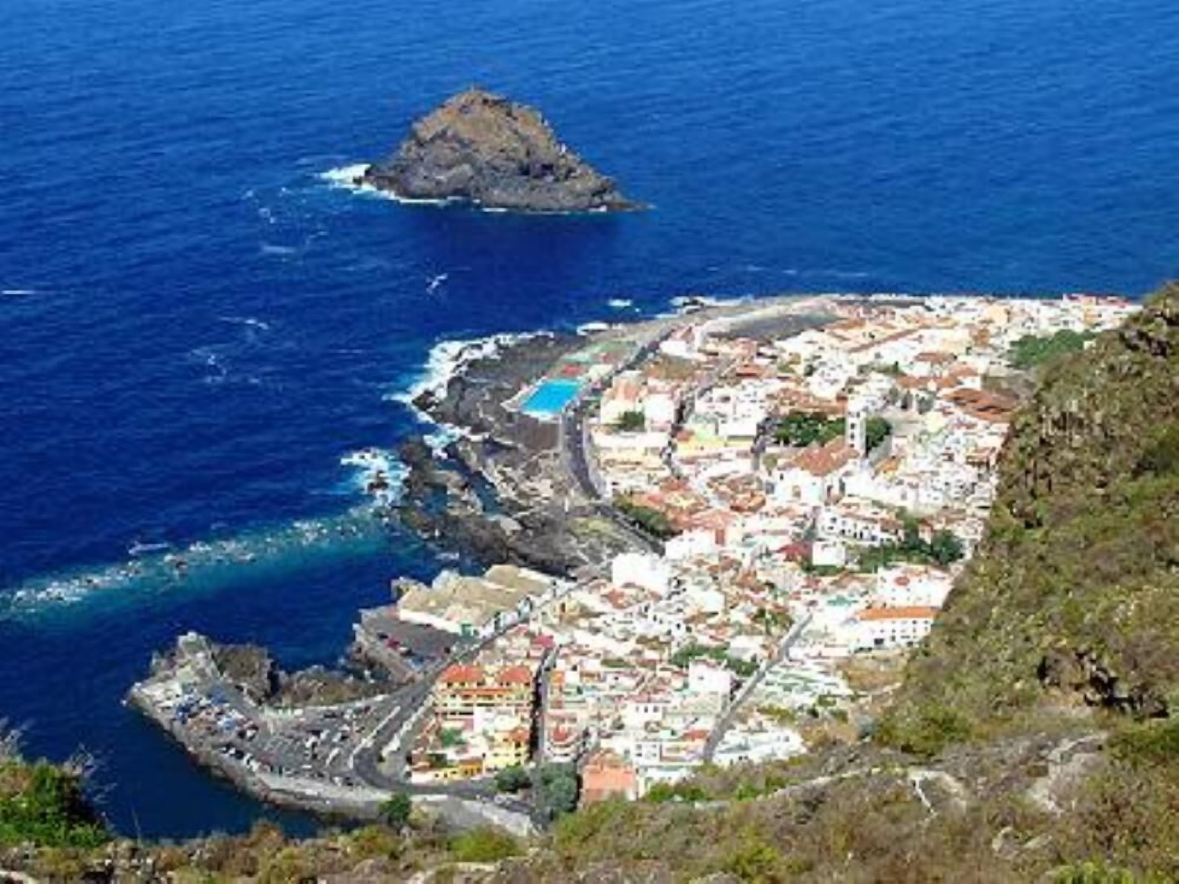 A coastal town with a mix of buildings, a prominent rocky outcrop, and a clear blue sea.