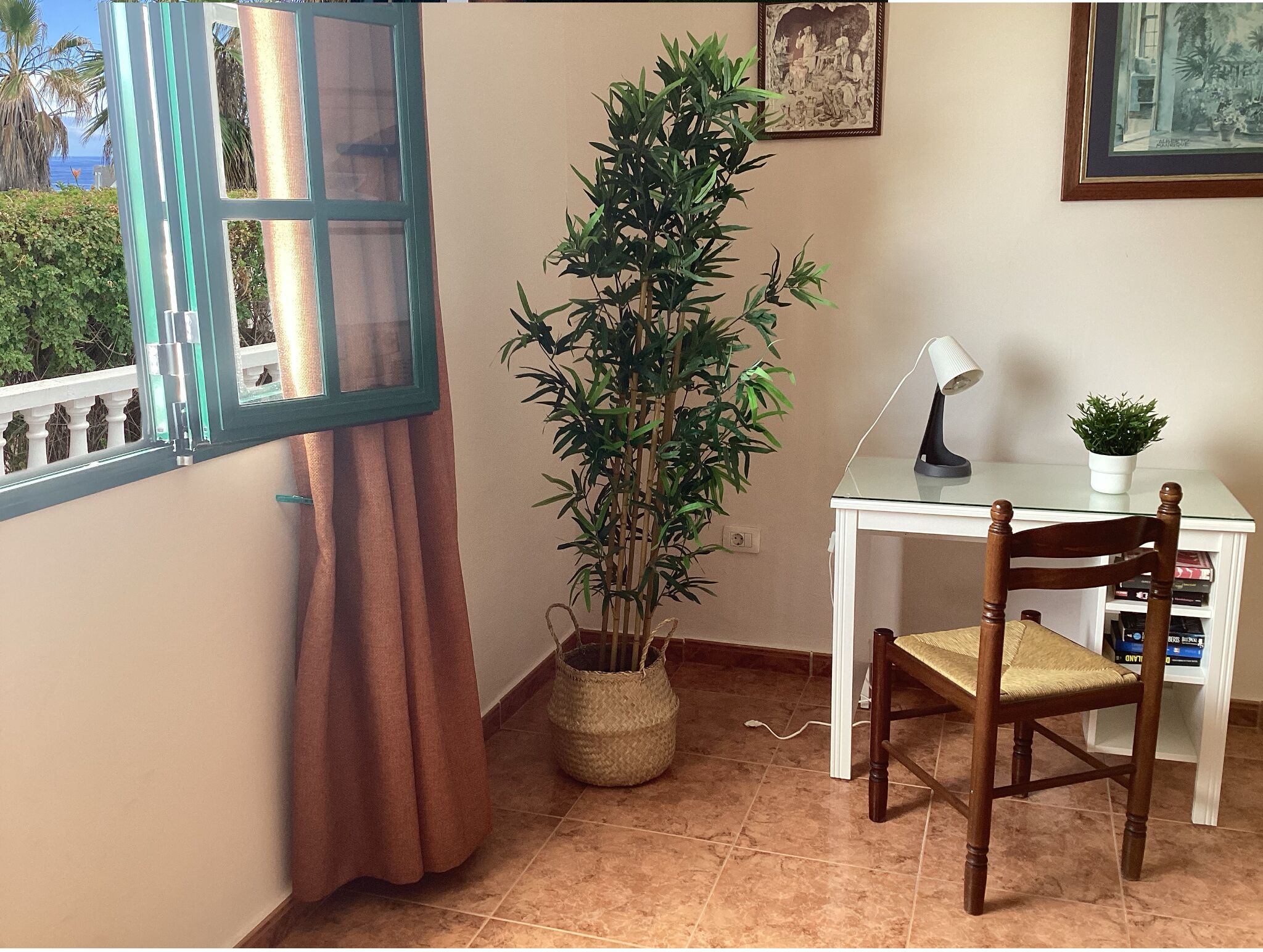 Una habitación con ventana, planta en maceta, escritorio con silla y lámpara.