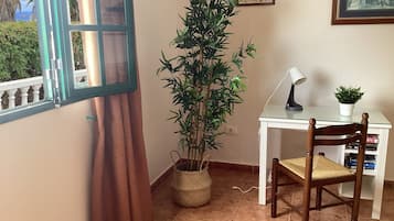 Una habitación con ventana, planta en maceta, escritorio con silla y lámpara.