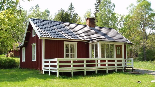 A red wooden house with a white porch and a chimney.