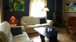 A living room with a glass coffee table, a beige sofa, a brown leather armchair, and a blue abstract painting on the wall.