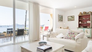 Un salon avec un canapé blanc, une table basse sur laquelle sont posés des livres et une vue sur la mer par une porte vitrée.
