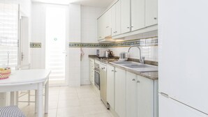 Une cuisine avec des meubles blancs, un évier, une cuisinière et un four à micro-ondes.