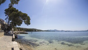 Une promenade en bord de mer bien aménagée, avec des escaliers en pierre menant à l’eau, une rangée d’arbres et une vue lointaine sur les bateaux et les collines.