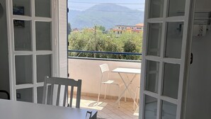 Ein Zimmer mit einem weißen Tisch und Stühlen, einem roten Sonnenschirm und Blick auf einen Berg und Gebäude.