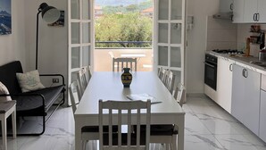 Eine moderne Küche mit weißen Schränken, einem Esstisch mit Stühlen und einem großen Fenster mit Blick auf Grünflächen und Berge.