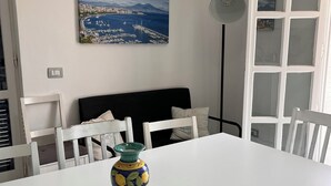 Ein Essbereich mit einem weißen Tisch, weißen Stühlen, einer Vase, einem Gemälde und einem Fenster mit weißem Rahmen.