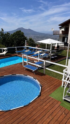 A swimming pool with a wooden deck, lounge chairs, and a view of a mountain.