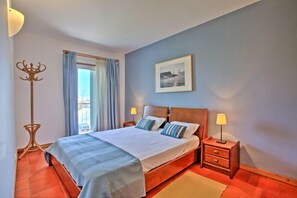 A bedroom with a bed, two bedside tables with lamps, a coat rack, a window with curtains, and a framed picture on the wall. - Apartment With Large Terrace Overlooking The Boats (Lagos)