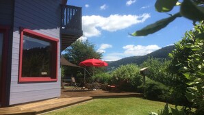 Une maison avec une fenêtre à cadre rouge, une terrasse en bois et un parasol rouge.