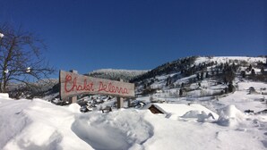 Un paysage enneigé avec un panneau en bois sur lequel on peut lire : « Chalet Delenna ».