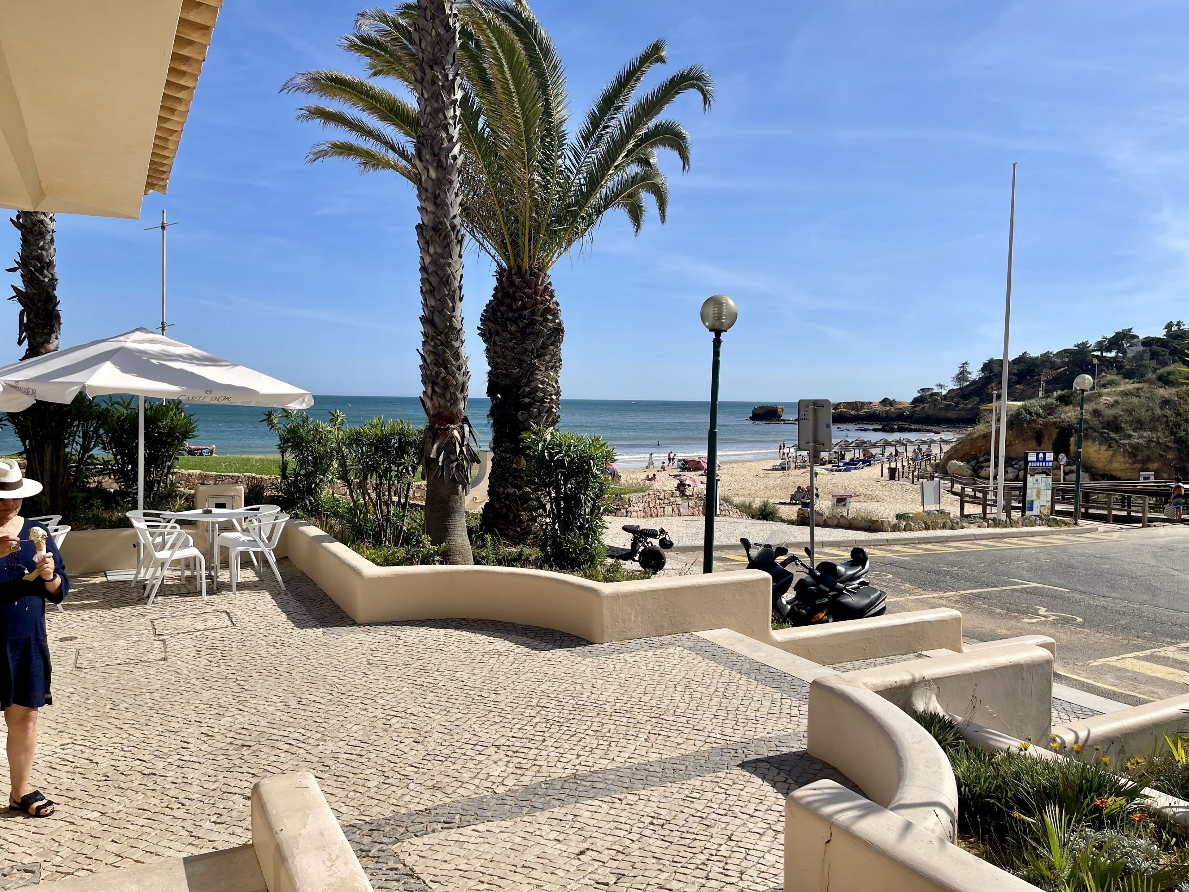 Un patio frente a la playa con palmeras, vista al mar y algunas scooters estacionadas.