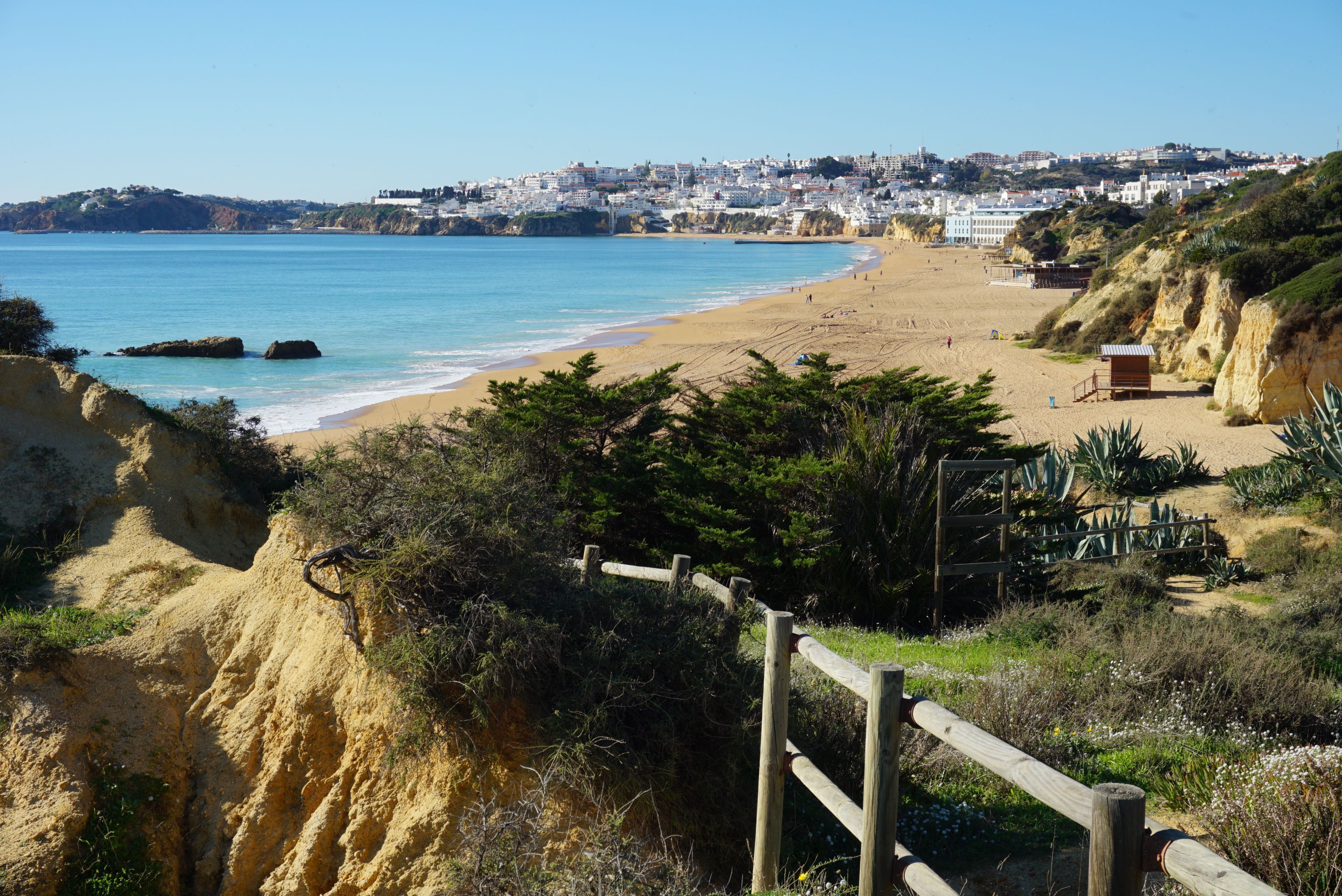 Une plage côtière avec une clôture en bois, un poste de surveillance pour les sauveteurs et une ville en arrière-plan.