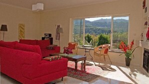 Un salón con sofá rojo, una mesita de centro y vistas a un paisaje montañoso a través de amplios ventanales.
