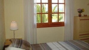 A bedroom with a bed, a nightstand, a lamp, a dresser, and a window with curtains. - sun and field (with wifi)  (Ariany)