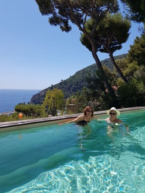 Ein Schwimmbecken mit klarem Wasser, umgeben von Bäumen und Blick auf das Meer.