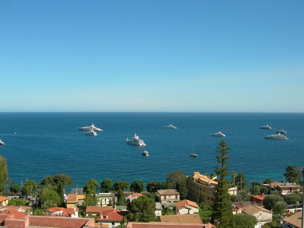 A coastal town with several yachts anchored in the sea, surrounded by residential buildings with red-tiled roofs.